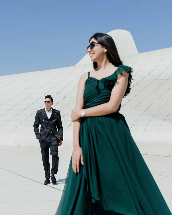 A candid moment of joy against the futuristic curves of the Heydar Aliyev Center in Baku. The contrast between her flowing green dress and the stark white architecture creates a visually stunning pre-wedding portrait.