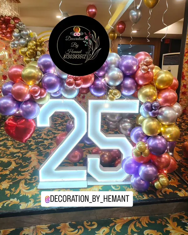 A close-up of the large, illuminated "25" marquee numbers used for a silver jubilee anniversary. The numbers are the centerpiece, surrounded by a lush arch of metallic purple, red, and gold balloons.