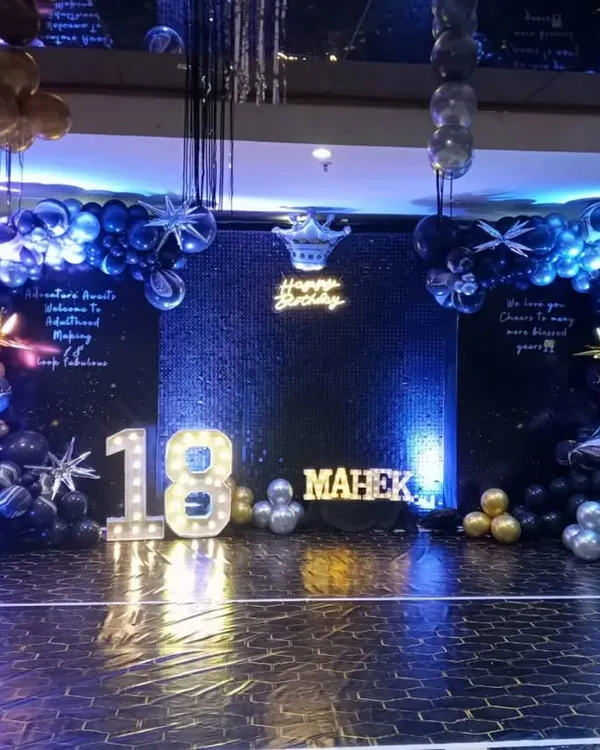 A grand and glamorous 18th birthday setup. The decoration features a dark, starry theme with a large dance floor, marquee numbers, and a balloon arch in shades of blue, black, and silver.