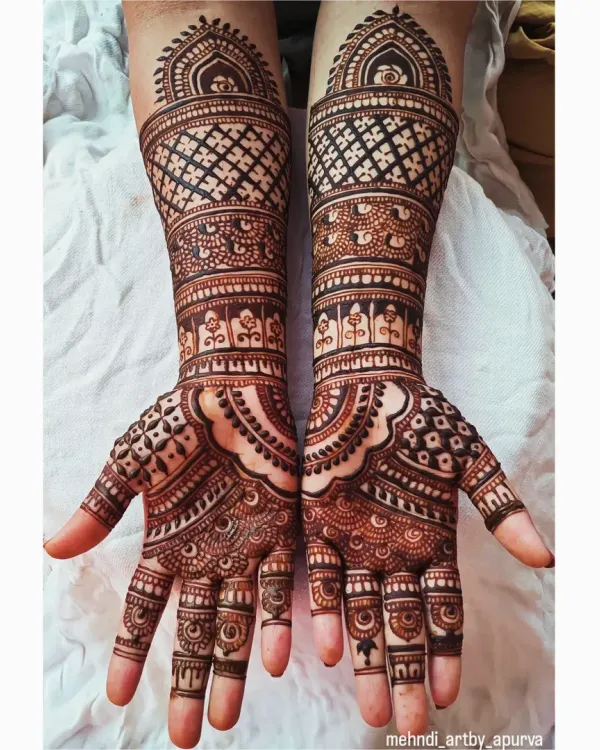 This symmetrical bridal design features a mix of geometric grids and traditional patterns. The careful balance between bold shapes and fine details creates a stunning effect that covers the hands and forearms.
