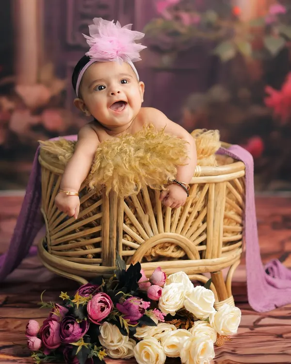 A beautiful baby portrait capturing a bright, happy expression. This simple studio setup with a wicker bassinet and flowers puts all the focus on her adorable smile.