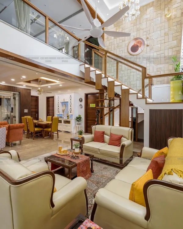 A grand, double-height living space in a penthouse, with a prominent staircase featuring a glass railing and stone-clad wall.