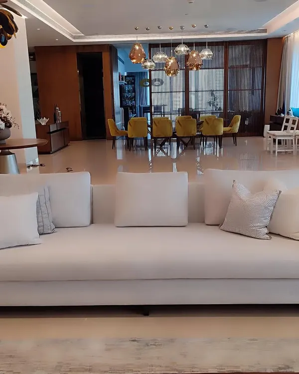 This expansive, timeless white sofa serves as the serene centerpiece of a luxurious open-plan living area. Its clean lines and generous proportions are complemented by an array of textured white cushions, demonstrating our ability to create foundational pieces that exude quiet, sophisticated luxury.