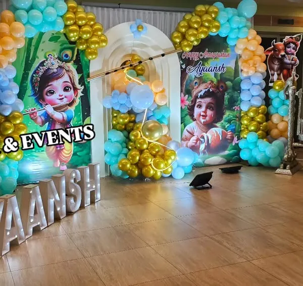 Another angle of the Little Krishna naming ceremony, showing how the balloon columns and character cutouts frame the main stage. The light-up marquee letters add a beautiful glow to the entire setup.