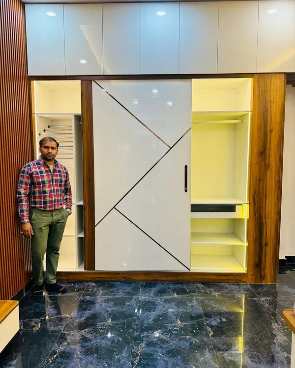 This is a floor-to-ceiling sliding wardrobe with a modern geometric design on the shutters. The combination of high-gloss white and wood finish gives the room a spacious and elegant feel.