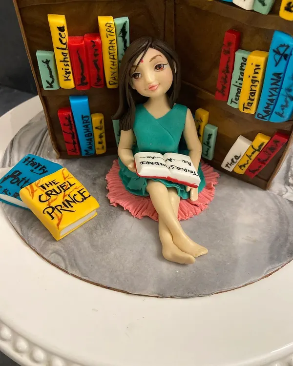 I made this cake for a young book lover. The figurine is personalized to capture her likeness, surrounded by tiny, edible versions of her favorite books.