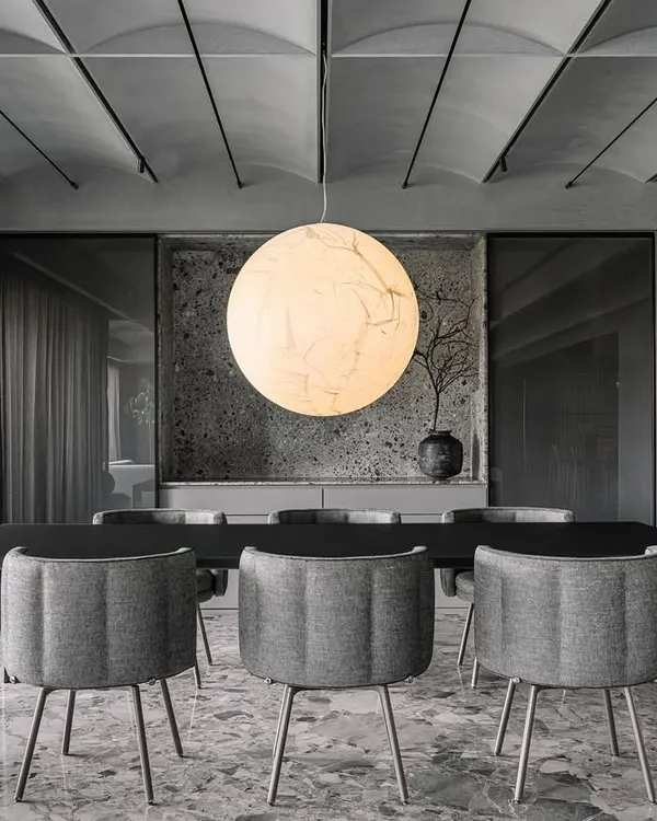 The 'Moon' pendant by Davide Groppi serves as the central anchor in the Vaulted Haus dining area. Its large, spherical form provides a soft, diffused light that holds the entire monochromatic space together under the vaulted ceiling.