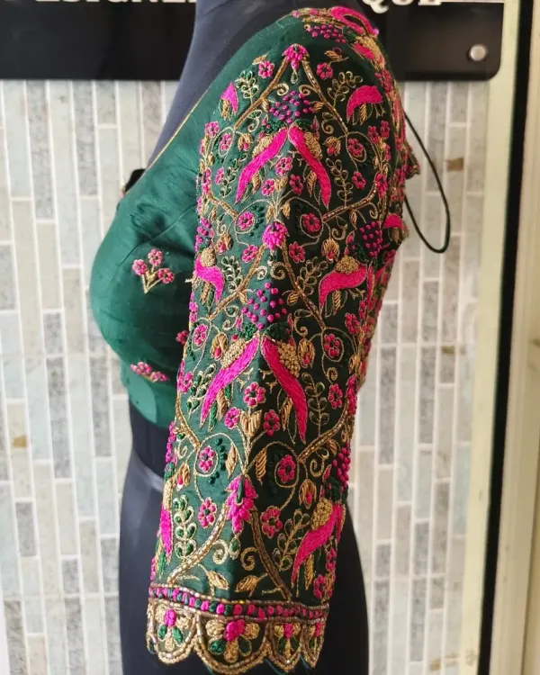 A side view showcasing the incredibly dense embroidery on the sleeve of this emerald green blouse. The vibrant pink and gold threads create a stunning contrast against the dark fabric.