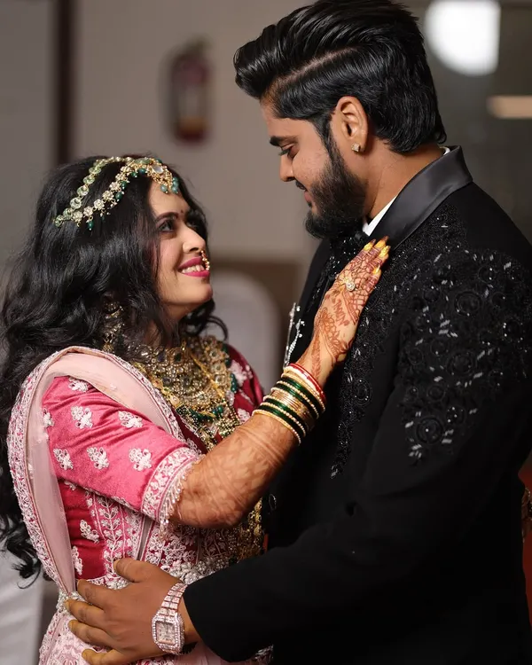 A sweet, romantic moment between the couple. The bride's makeup is soft and glowing, perfect for an engagement ceremony, complementing her pink lehenga beautifully.