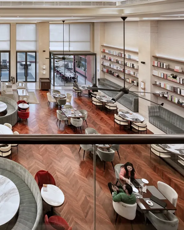 A high-angle view of the Elevate Clubhouse in Gurugram, showcasing the expansive, double-height living and dining area. The design emphasizes visual connectivity and a sophisticated yet comfortable atmosphere, with herringbone wood flooring and curated furniture layouts that encourage social interaction.