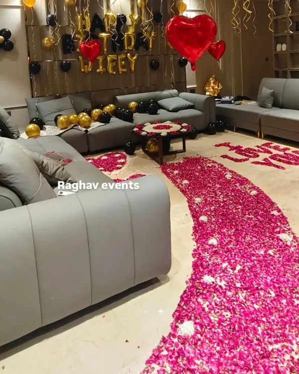 A grand romantic gesture for a wife's birthday. This living room decoration includes a rose petal pathway, 'I LOVE YOU' written on the floor, and a 'Happy Birthday Wifey' balloon setup.
