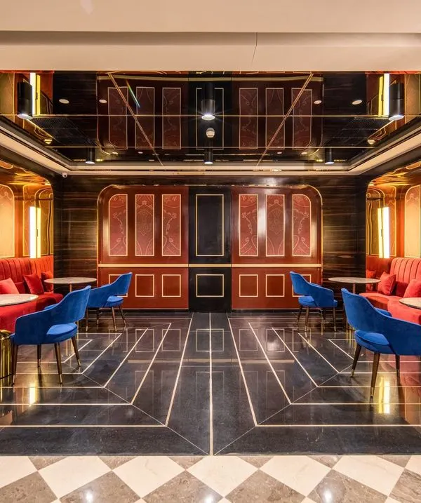 This private lounge area at INOX, Rajouri Garden, offers a luxurious pre-movie experience. The design uses rich red velvets, dark wood paneling, and a reflective ceiling to create an intimate and opulent atmosphere, reminiscent of classic Hollywood glamour.