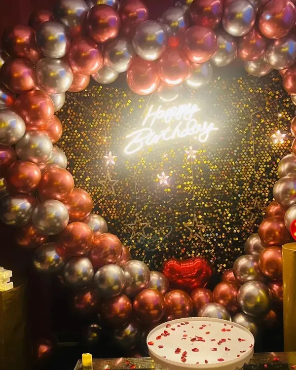 A classic birthday setup featuring a heart-shaped arch with red and silver chrome balloons, a 'Happy Birthday' neon sign, and a cake stand ready for the main event. This is one of my most requested romantic birthday themes.