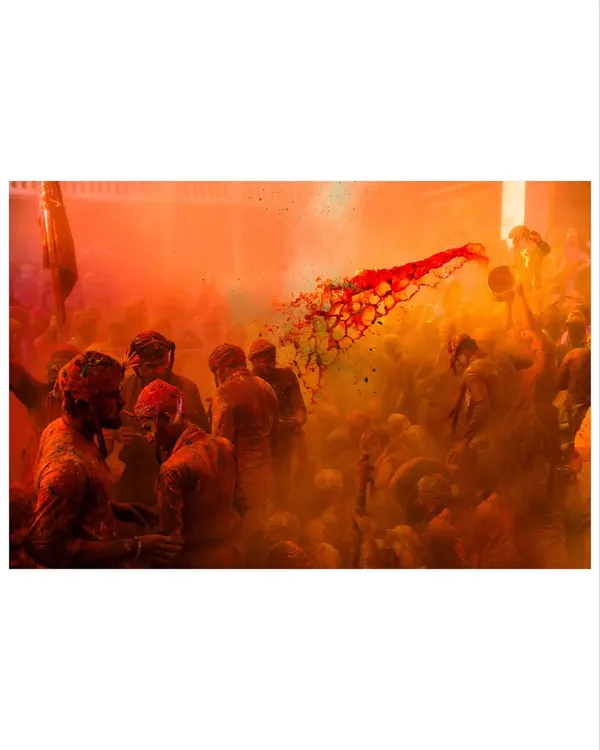 A jet of red color explodes through a cloud of orange powder during Holi. Capturing these split-second moments of action is what makes festival photojournalism so thrilling.