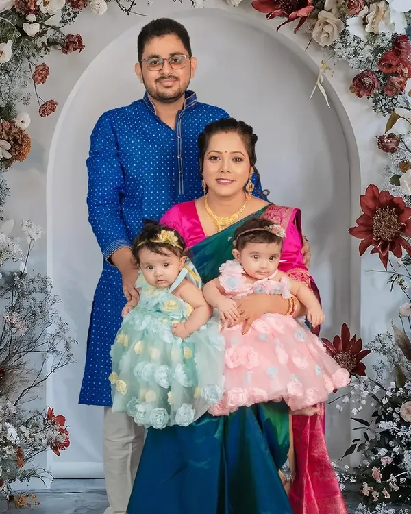 A lovely family portrait with their twin toddler girls. Dressed in beautiful traditional and party wear, the family is framed by a stunning floral arch, creating an elegant and memorable photograph.