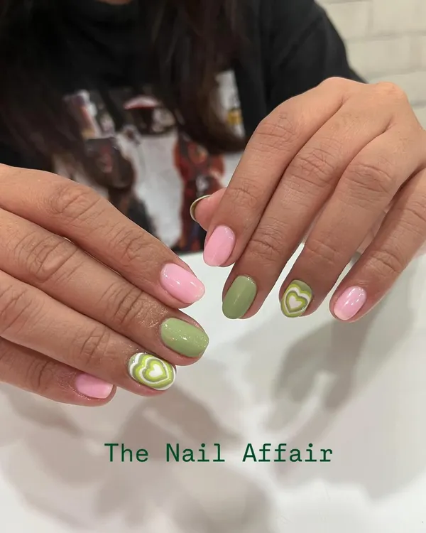 A cute and trendy design combining pastel pink and sage green nails. The accent nails feature a fun, hand-painted heart swirl pattern for a playful touch.