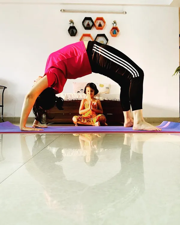 I believe in leading by example. Here, while I hold Chakrasana, a young student finds her own center in a simple prayer pose. This is the heart of my teaching: creating a space where children can watch, learn, and grow at their own pace, finding their own expression of yoga.