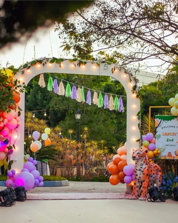 A grand entrance arch welcomes guests to Saachi's 2nd birthday, featuring life-sized animal props, lush greenery, and warm lighting for a magical evening safari.