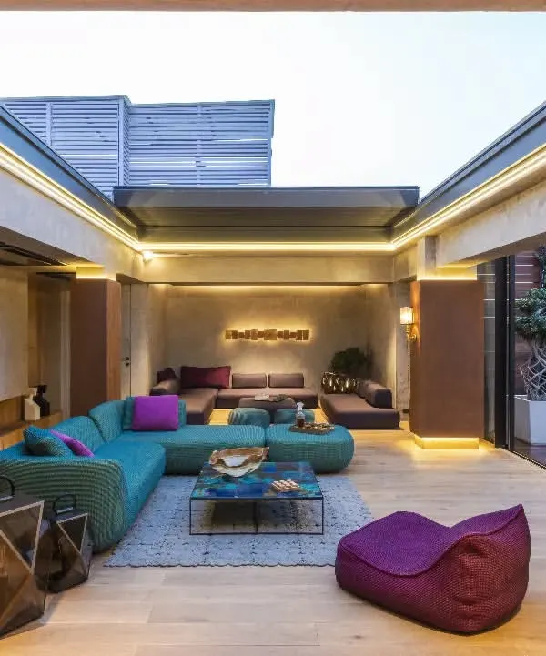 A wide view of the vibrant lounge in a New Delhi residence. The space is designed for entertainment, featuring eclectic furniture and a retractable roof that opens up to the sky, seamlessly connecting the indoors with the outdoors.