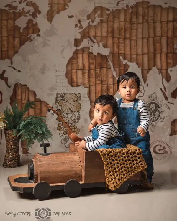 Twin boys ready for a journey in this travel-themed setup. The world map backdrop and wooden train prop create a sense of adventure for their combined photoshoot.