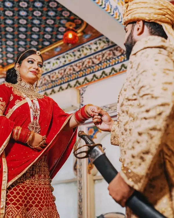 A moment of royal connection inside a beautifully ornate Udaipur palace. The groom, dressed in a classic sherwani, gently holds his bride's hand, showcasing the elegance and heritage of a Rajasthani theme.