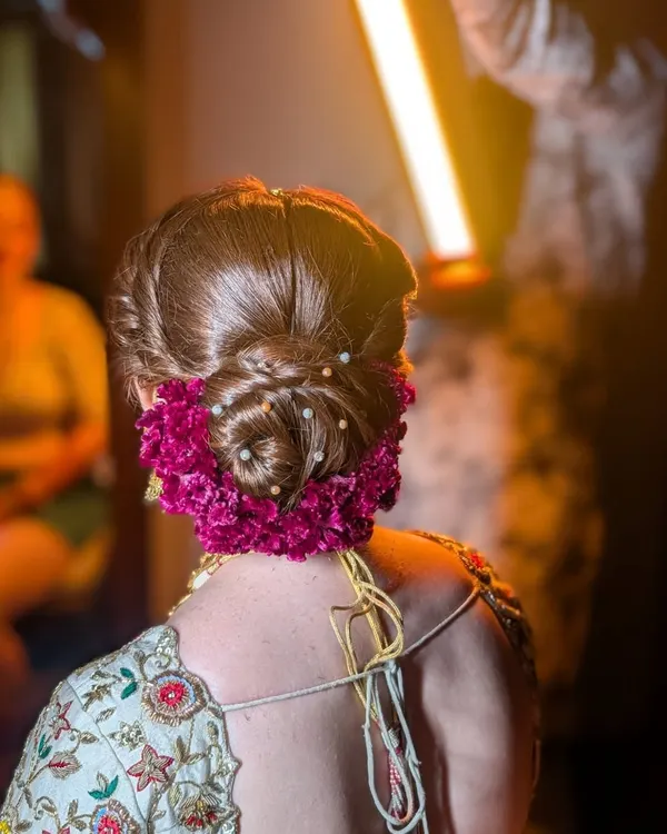 A stunning floral bun, perfect for a bride or any special occasion. This intricate updo is adorned with fresh magenta flowers and delicate pearls, creating a look that is both romantic and elegant.