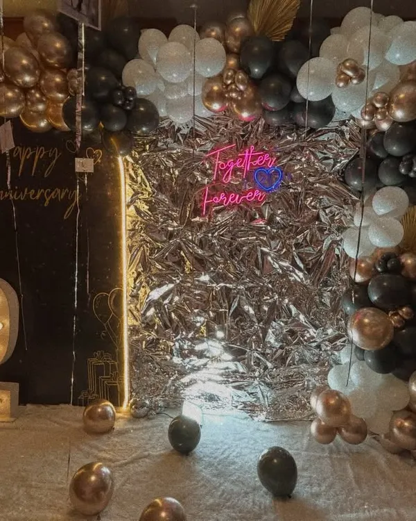 Our 'Bling Bling' decor is perfect for adding glamour to any anniversary. This setup features a stunning silver foil backdrop, a 'Happy Anniversary' neon sign, a light-up number '2', and a black, white, and rose gold balloon garland.