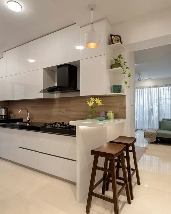 A look at a modern kitchen renovation we completed, designed for seamless cooking and entertaining. This space features handleless glossy white cabinets for a clean, minimalist look, a functional breakfast counter for casual meals, and a warm wood-textured backsplash. We focus on smart layouts that combine high-end appliances with ample storage and workspace.