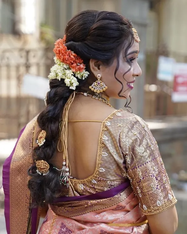 A detailed back view of a contemporary bridal braid. This style combines traditional braiding techniques with modern sensibilities, using both flowers and classic hair accessories to match the bride's Kanjivaram saree.