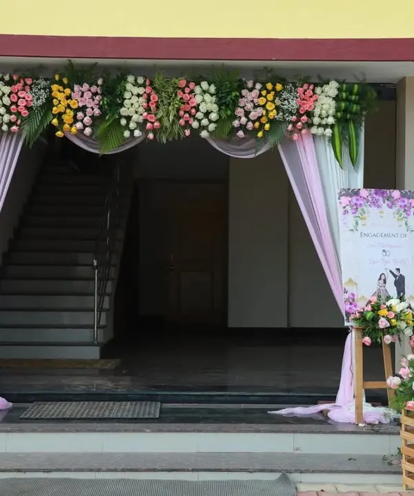A beautiful entrance for an engagement ceremony. The arch is decorated with pastel flowers and soft pink drapes, with a welcome board and floral crates greeting the guests.