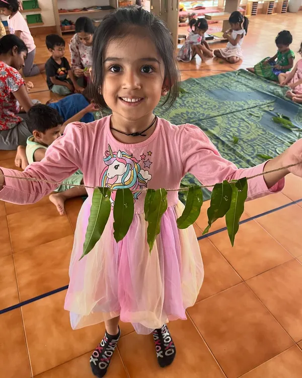 A smiling child shows off the 'thoran' she made from leaves during summer camp. Our camp activities are often inspired by nature and hands-on creativity.