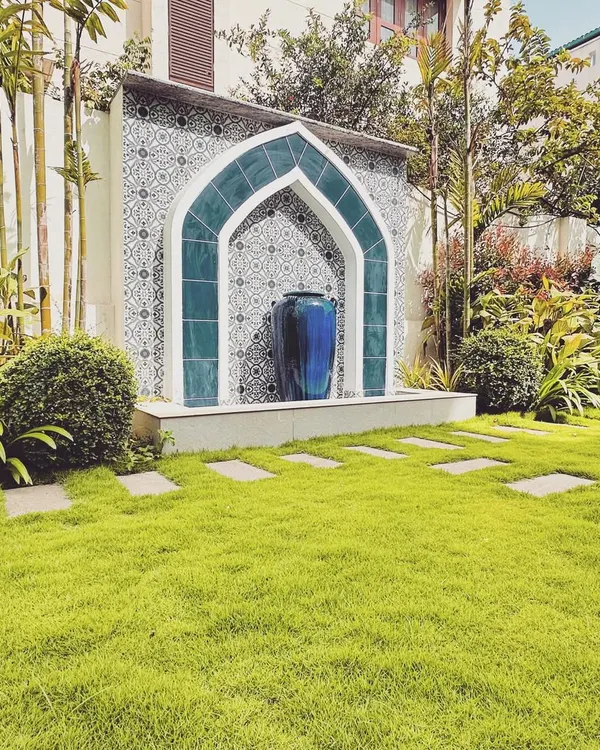This Moroccan-inspired water feature serves as the breathtaking centerpiece of a lush garden. The intricate tilework, deep blue arch, and elegant urn create a focal point that is both sophisticated and tranquil, perfectly framed by a manicured lawn and stone pathway.