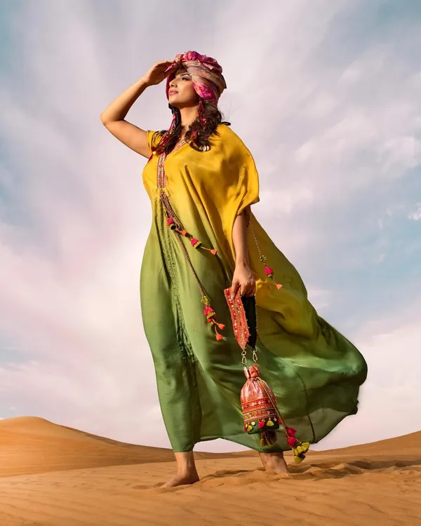 A powerful pose in the desert, with the model looking towards the horizon. The vibrant colors of the kaftan and turban stand out beautifully against the blue sky.