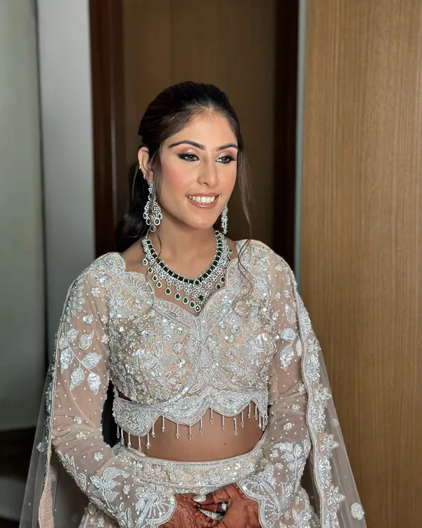 A sangeet bridal vision in an ivory and shimmer lehenga. This look features soft pink eyeshadow, a flawless base, and a natural lip color.