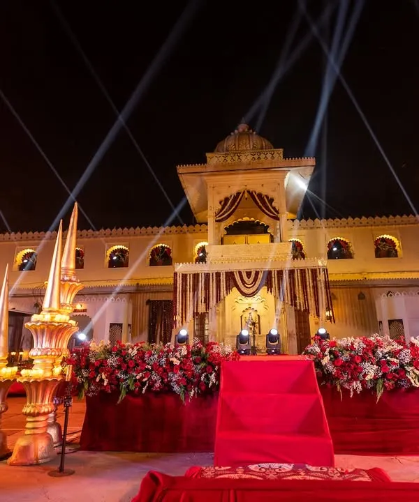 A grand stage setup for a Sangeet at Jagmandir, featuring regal decor, bold red florals, and dramatic spotlights to create a powerful focal point for the evening's performances.
