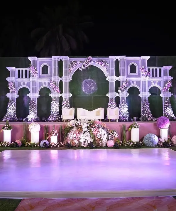 This grand stage, with its palatial white arches and delicate floral accents, was designed to be the perfect royal backdrop for the wedding couple. The elevated platform and soft lighting ensure all eyes are on them.