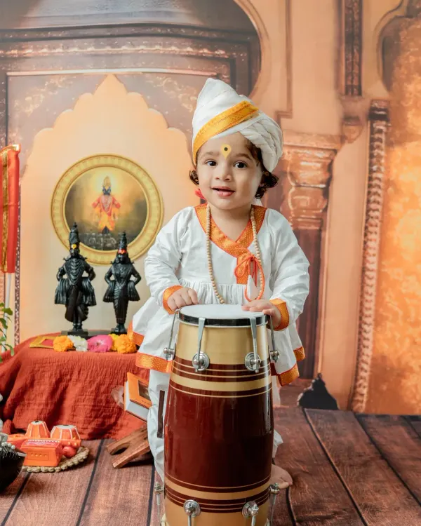 A joyful moment from a 'Chota Varkari' shoot, where the baby boy stands with a traditional pakhawaj drum. The authentic turban and attire complete this cultural portrait.