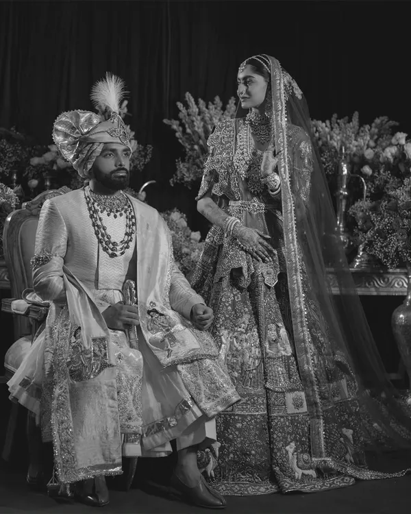 A regal portrait in monochrome. This black and white image of the couple has a timeless, classic feel, emphasizing the rich textures of their traditional attire and the gravity of the moment.