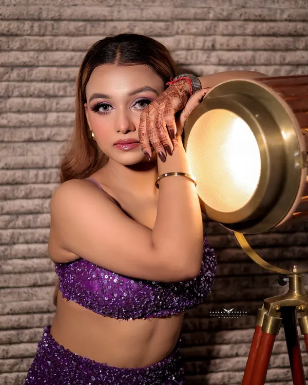 A creative studio portrait where the model leans against a vintage spotlight, creating a warm glow on her face.