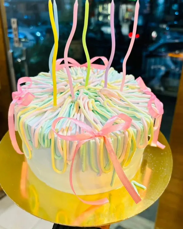 A close-up of one of my custom-designed pastel ribbon cakes. This style is popular for birthdays and celebrations, complete with whimsical, wavy candles.