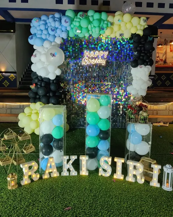 This birthday setup features a multi-colored balloon arrangement against a glittering shimmer wall. I also included light-up letters for the name and clear plinths filled with balloons for a unique touch.