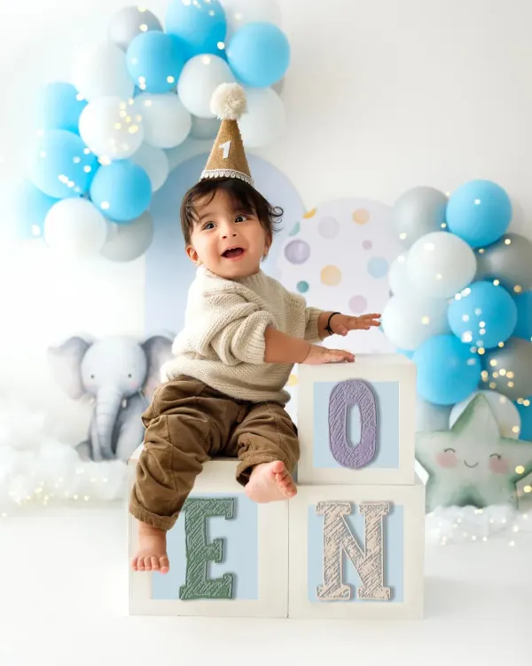 He's ONE! This little boy is celebrating his first birthday, sitting proudly on top of "ONE" blocks. The blue and white balloon arch adds a festive touch.