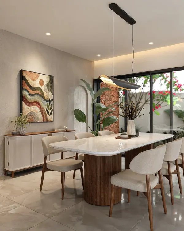 A contemporary dining space featuring a marble-top table with a fluted wooden base. The room is accented by an abstract artwork and a large plant, with glass doors opening to an outdoor area.