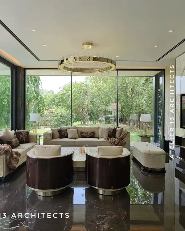 This glass house lounge, designed for a private farmhouse in Vasant Kunj, Delhi, blurs the line between indoors and out. The space features a dark marble floor that reflects the lush garden views, a statement ring chandelier, and custom revolving chairs, creating an environment of seamless modern luxury.
