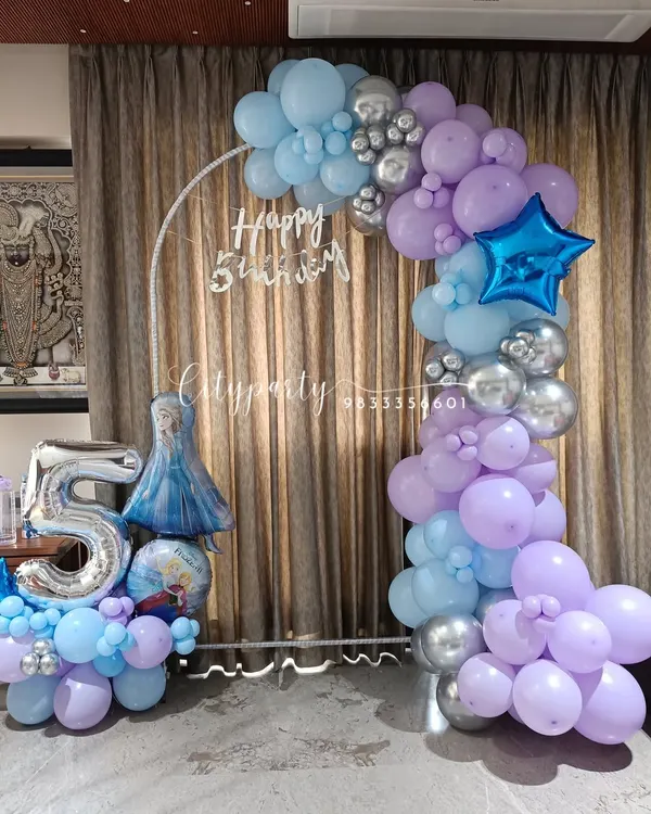A 'Frozen' themed balloon arch for a 5th birthday, designed with pastel blue, purple, and chrome silver balloons. The setup includes a large '5' foil balloon and an Elsa character balloon.