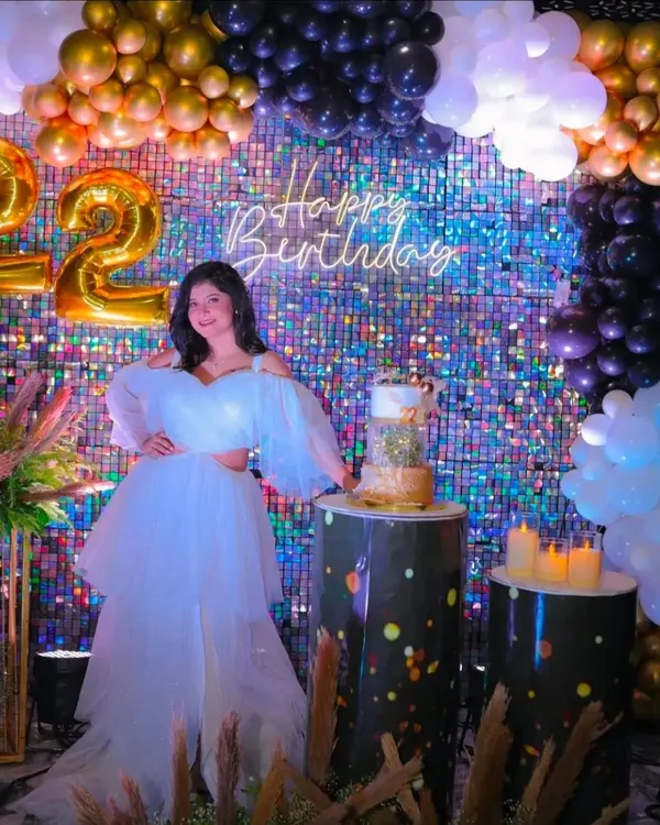 A stunning 22nd birthday celebration with a shimmering sequin backdrop. The decor is elevated with a black and gold balloon garland, foil number balloons, and custom-printed pedestals for the cake.