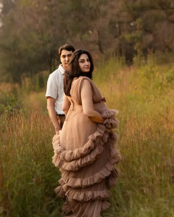 A flowing gown in a rustic, sun-drenched field creates such a dreamy atmosphere for a maternity shoot. This portrait captures a moment of quiet connection as the couple looks toward their future together.