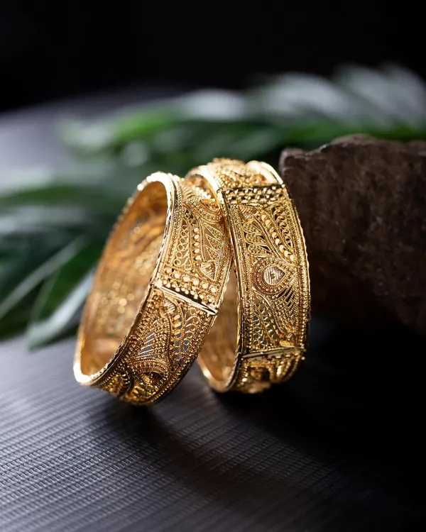 A detailed product shot of intricately designed gold bangles. I used a rock and natural leaf to create an earthy, rustic setting that contrasts beautifully with the polished gold.