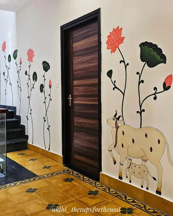 This wide shot shows how the Pichwai mural, with its cow-calf motif and climbing lotuses, elegantly frames the doorway and complements the traditional Indian flooring.