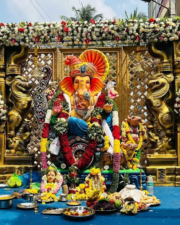 A grand Ganesh Chaturthi pandal we created for a community celebration. The setup features a majestic Ganesha idol set against an ornate gold lattice backdrop, flanked by traditional Yali pillars and adorned with lush garlands of white and red flowers.